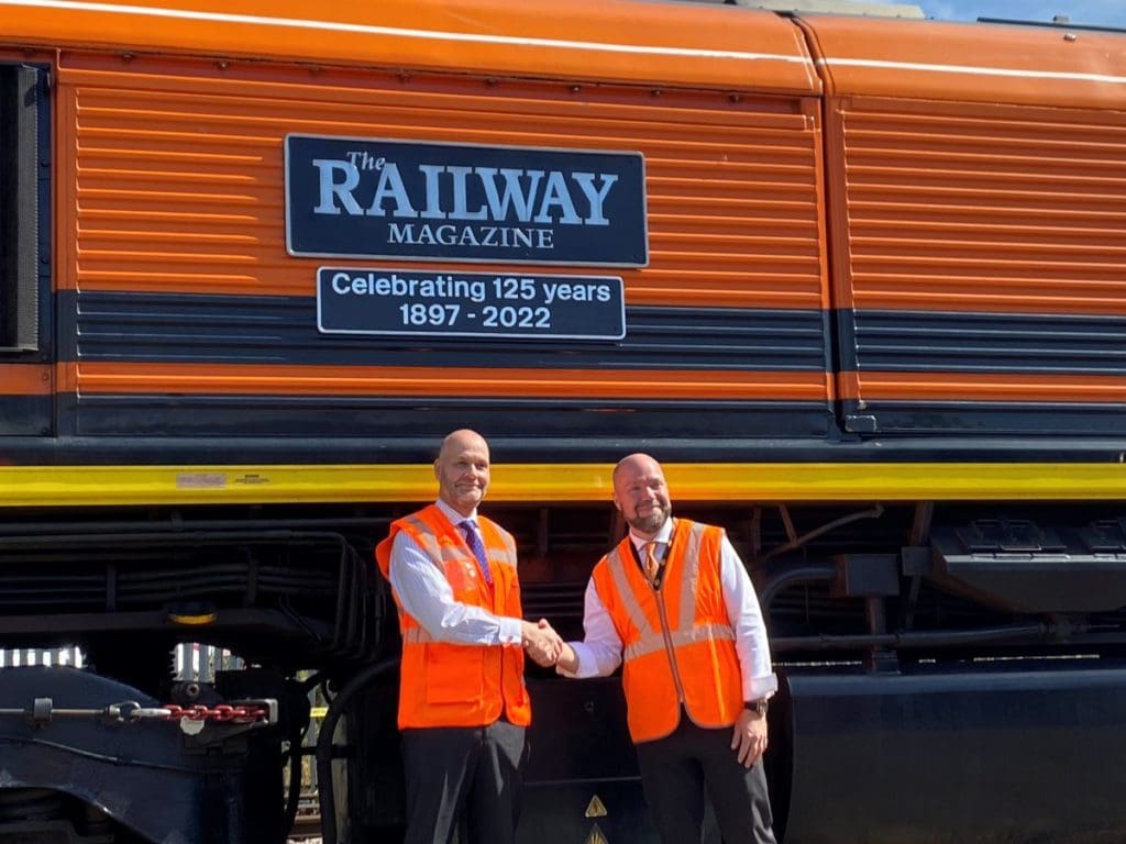 Paul and Blake shake hands in front of the loco with the nameplates "The Railway Magazine" and "Celebrating 125 years 1897-2022."